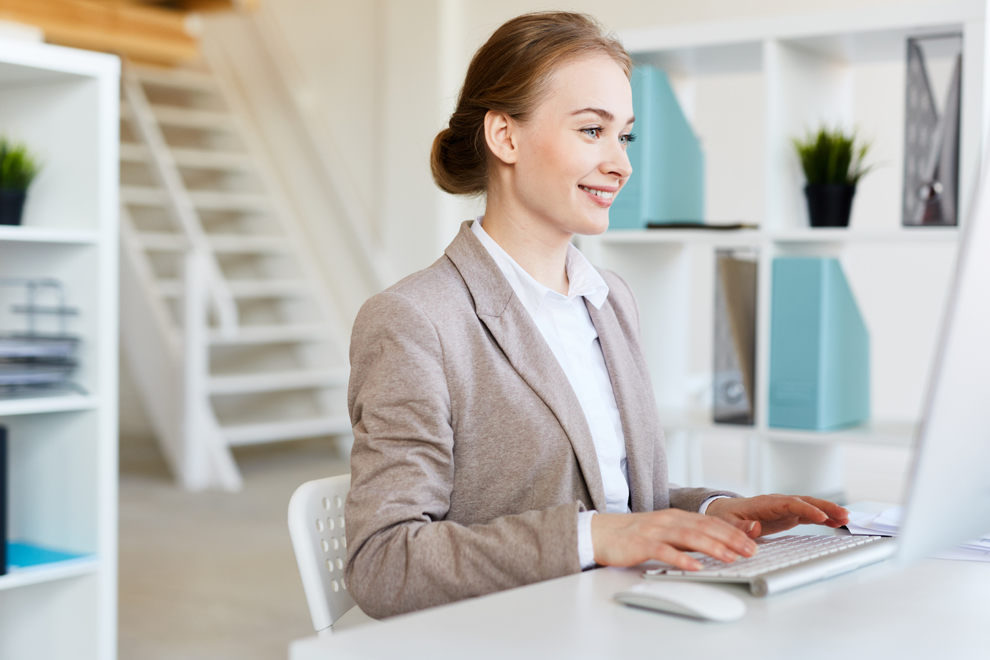 Attractive young entrepreneur writing response e-mail to her business partner while sitting in front of computer, interior of modern office on background